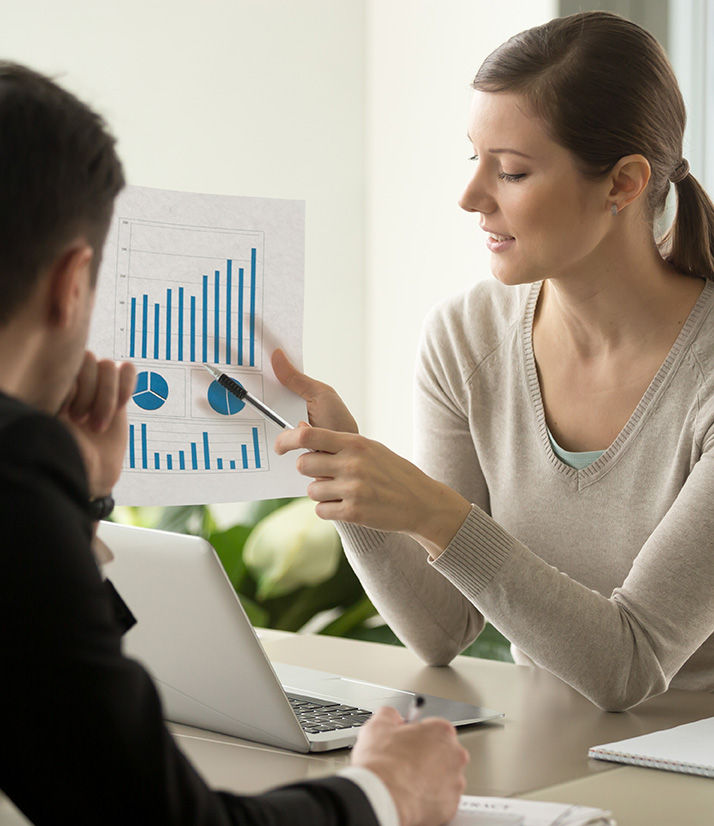 Attractive millennial businesswoman presenting company financial indicators, telling business partner about investment plan, showing document with project positive stats sitting at office desk