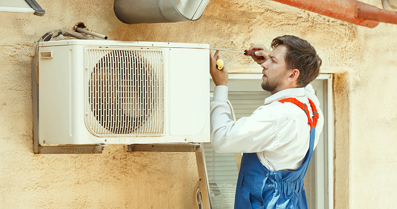 HVAC technician working on a capacitor part for condensing unit. Male worker or repairman in uniform repairing and adjusting conditioning system, diagnosting and looking for technical issues.