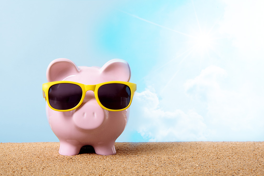 Pink piggy bank on a beach with yellow sunglasses.  Space for copy. Travel money concept.